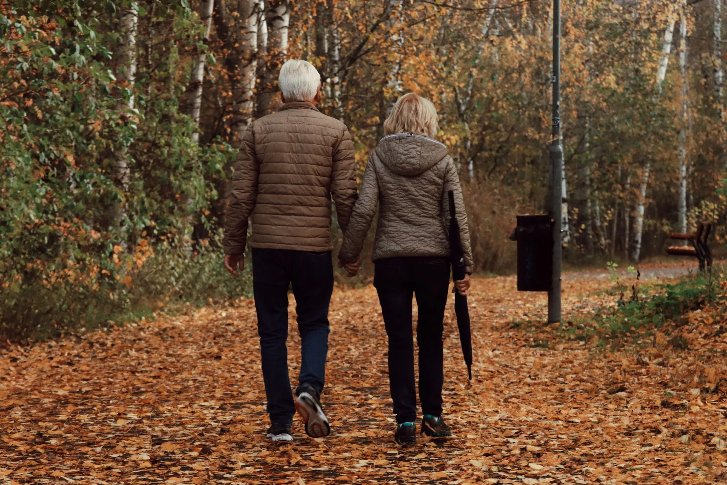 Senior couple enjoying a peaceful walk through a leafy park in Jönköping, Sweden during autumn.