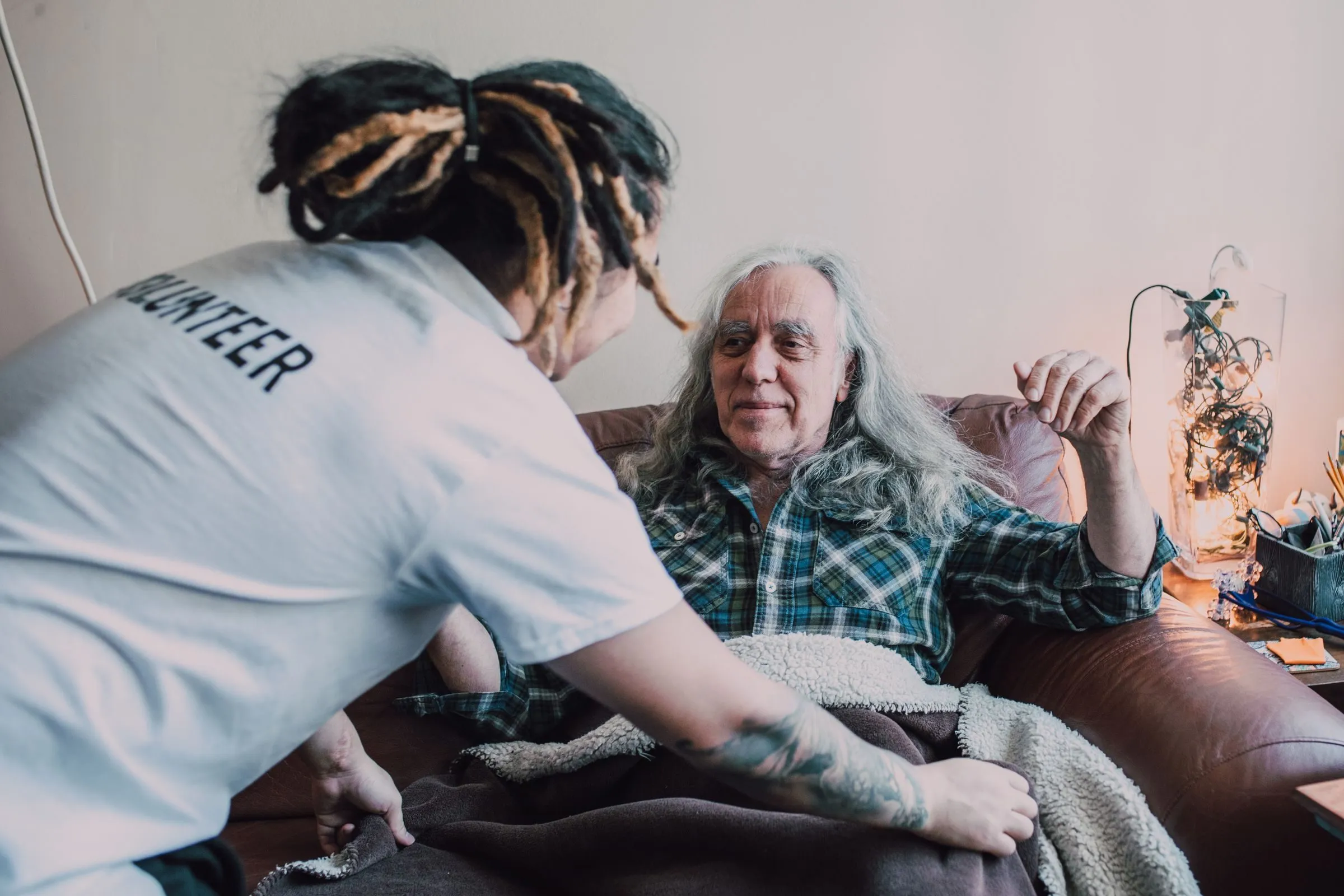 Volunteer helps an elderly man relax at home, promoting charity and care.
